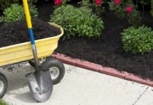 Wheelbarrow and shovel beside a flower bed with brick landscape edging