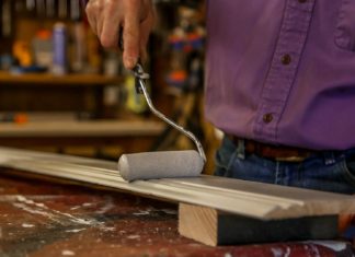 Painting wooden baseboard with a foam trim roller in a workshop.