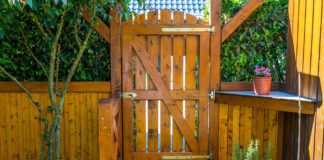 Tall wooden fence gate leading to a beautifully landscaped patio