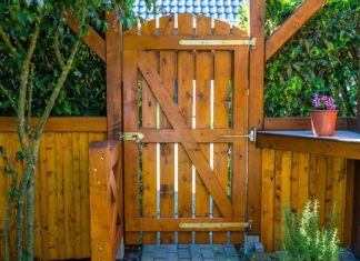 Tall wooden fence gate leading to a beautifully landscaped patio