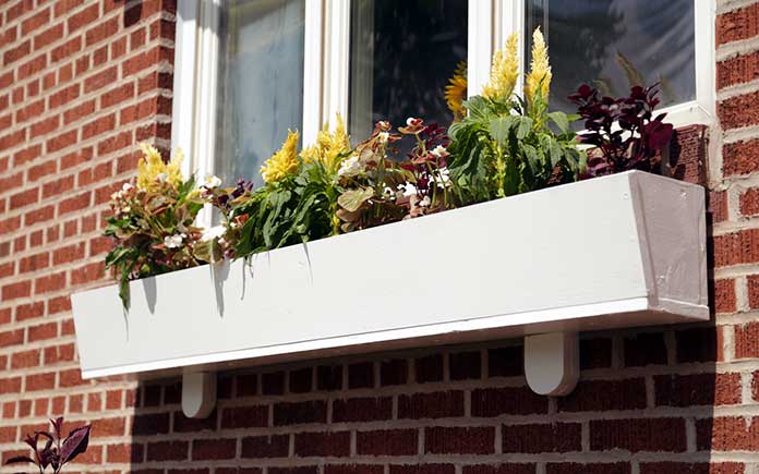 A homemade wooden window box installed under a window on a brick home