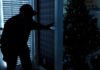 Burglar entering home with lights off and nearby Christmas tree