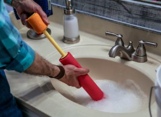 Joe Truini siphons standing water from a bathroom sink with a water toy