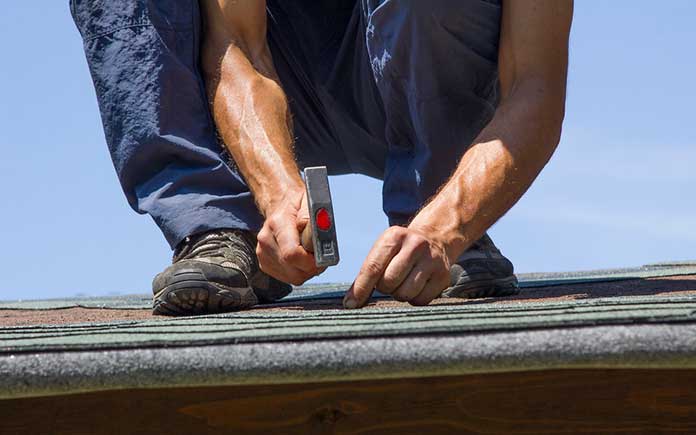 Man hammering a nail into an asphalt shingle on the roof