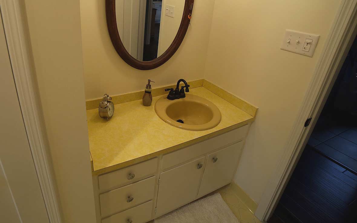 Yellow bathroom with dated vanity and cabinets