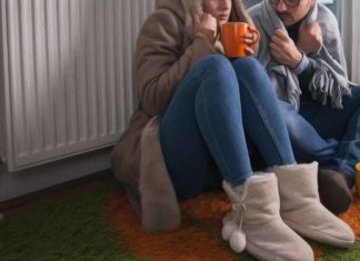 Cold couple sitting near radiator, bundled up and trying to get warm