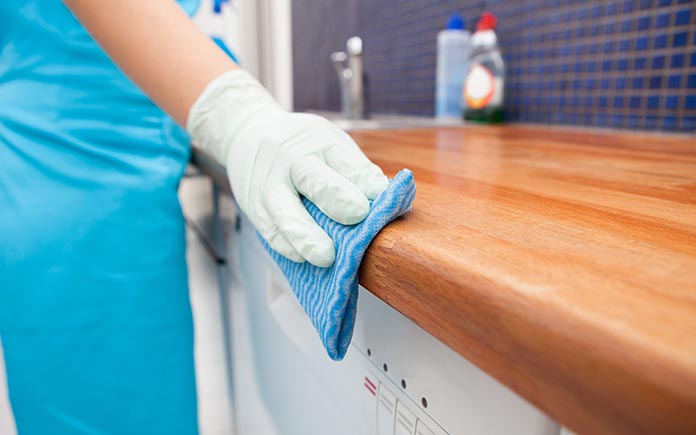 Scrubbing a butcher block countertop with a gloved hand and a sponge