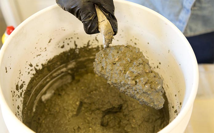 Concrete mix scooped out of a plastic bucket with a trowel and appearing like pancake batter