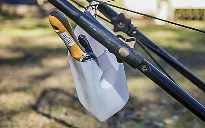Milk carton made into a holster for various gardening tools hangs on a lawnmower's handle