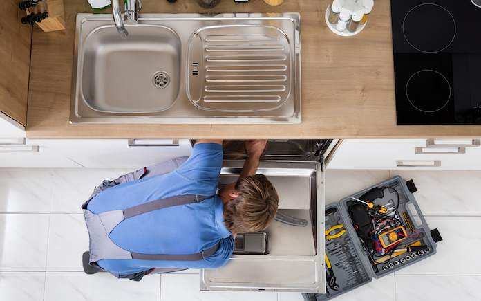 High Angle View Of Man In Overall Repairing Dishwasher In Kitchen
