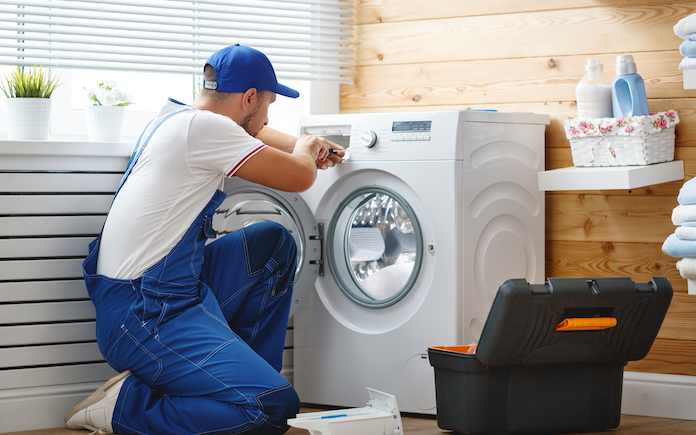 working man plumber repairs a washing machine in laundry
