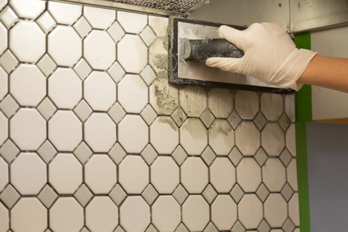 Gloved hand trowels grout over a tile backsplash