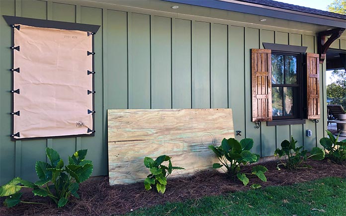 Hurricane fabric panel installed over a window, plywood hurricane shutter leaning against side of home, and working wooden shutters attached to a window