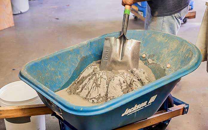 Man mixes concrete mix in a wheelbarrow with a shovel