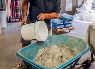 Man pours a bucket of water into the Quikrete countertop concrete mix in a wheelbarrow