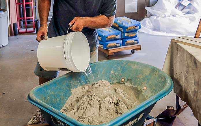 Man pours a bucket of water into the Quikrete countertop concrete mix in a wheelbarrow