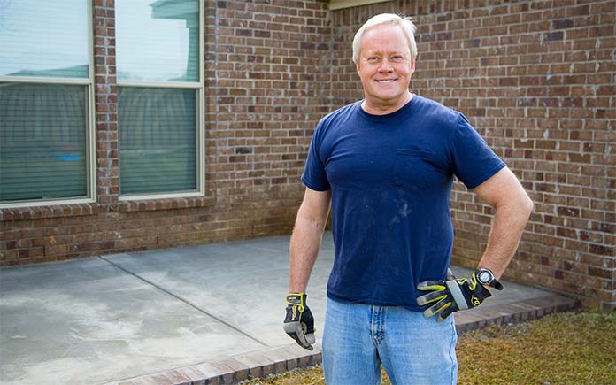 Danny Lipford, vêtu d'une chemise à manches courtes, se tient debout et sourit devant un patio en béton tout juste terminé