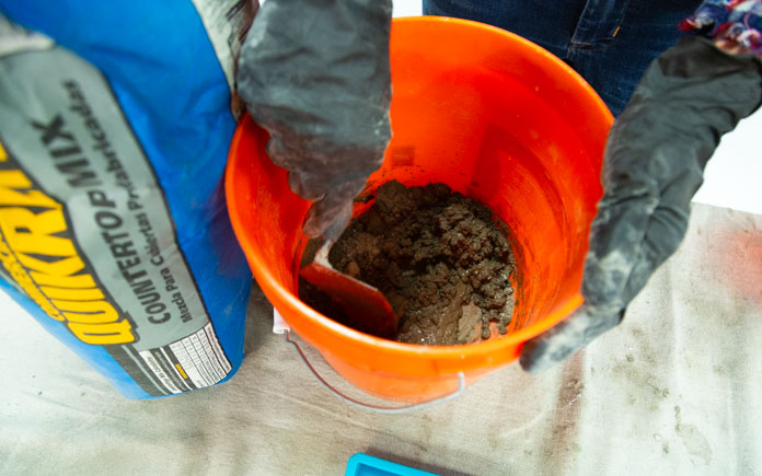 A gloved hand uses a masonry trowel to mix Quikrete Countertop Mix in an orange bucket