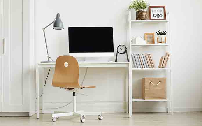 College dorm essentials including a desk, chair on rollers, desk lamp, clock and books