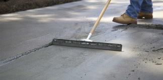 Man drags broom over wet concrete to give it a rough surface