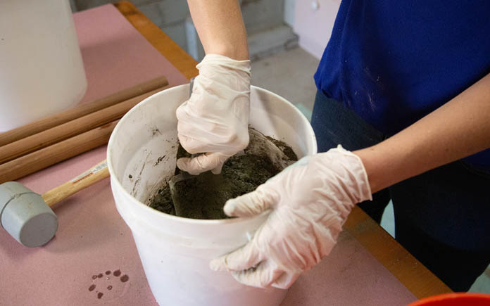 Gloved hand mixing Quikrete concrete with a masonry trowel in a white plastic bucket