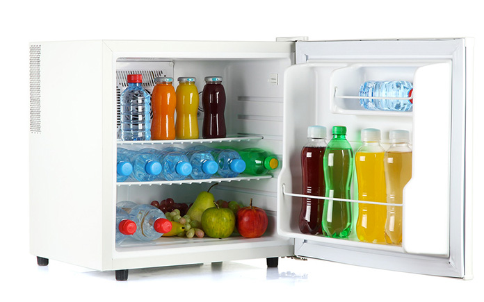 Mini réfrigérateur blanc pour un dortoir universitaire. Le réfrigérateur est rempli de jus de fruits assortis, de bouteilles d'eau et de fruits.