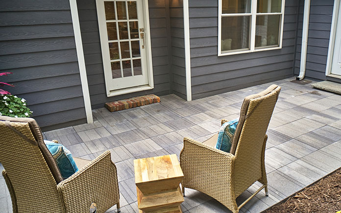 Pavestone Avant Linear pavers, seen on a patio viewed from behind two lounge chairs, facing a home's back entry