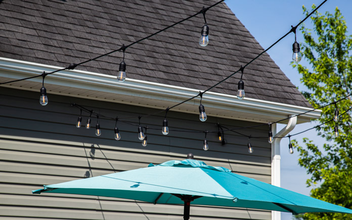 Cafe lights, seen over a patio umbrella near a home with vinyl siding