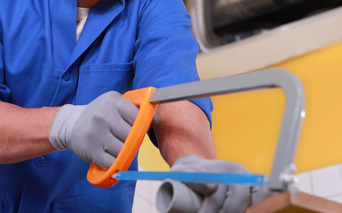 Man with gloved hands cuts pvc pipes with an orange hacksaw