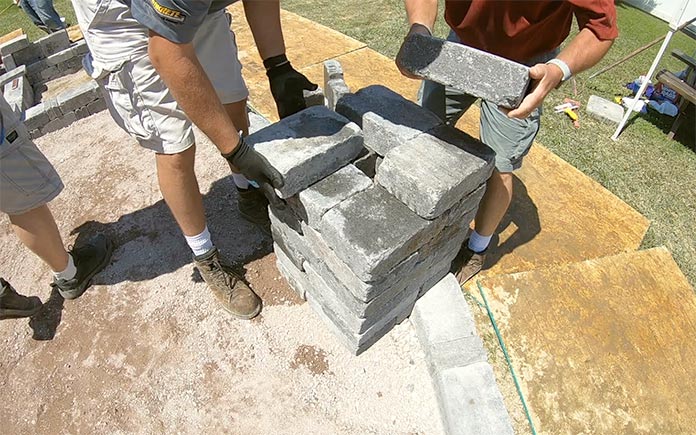 Men install pavers for the base of a light post on a paver patio
