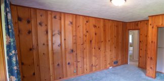 Dated wood paneling in a bedroom with unsightly carpeting