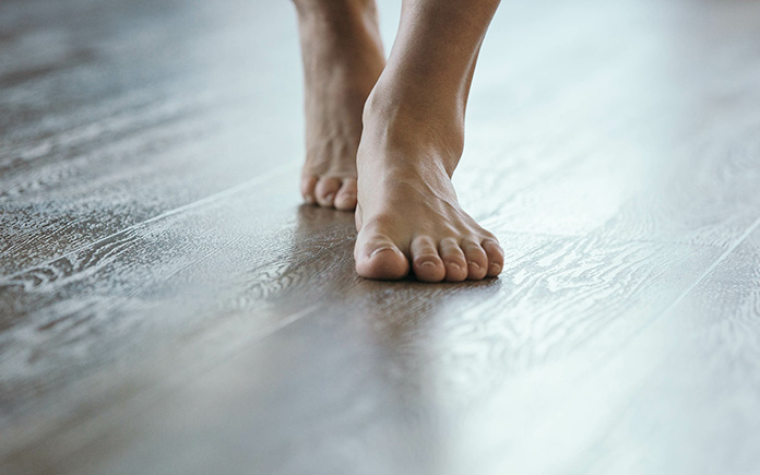 Bare feet, seen close up, walking on wood plank flooring installed over radiant heating system