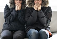 Couple, wearing parkas, shivering on their couch in their cold home during harsh fall weather