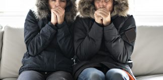 Couple, wearing parkas, shivering on their couch in their cold home during harsh fall weather