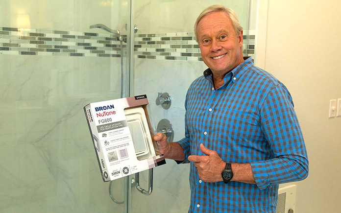 Danny Lipford, posé dans cette salle de bain à la maison, désigne une boîte avec un ventilateur Broan-NuTone qu'il installera dans sa douche personnelle.