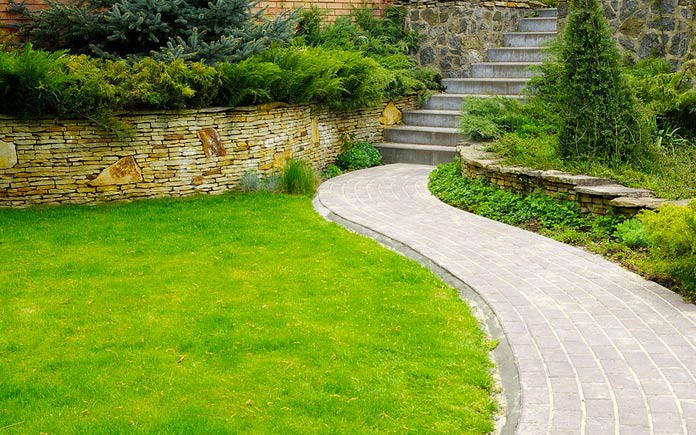 Lush backyard with stone path and retaining wall filled with plants and bushes