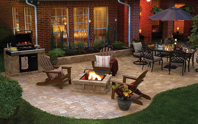 Brick home with a paver patio featuring a Pavestone RumbleStone fire pit, Adirondack chairs and an outdoor dining set with an umbrella