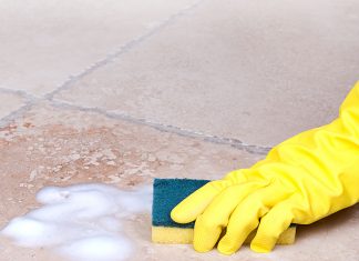 Gloved hand scrubbing ceramic tile floor with ammonia and liquid dish soap