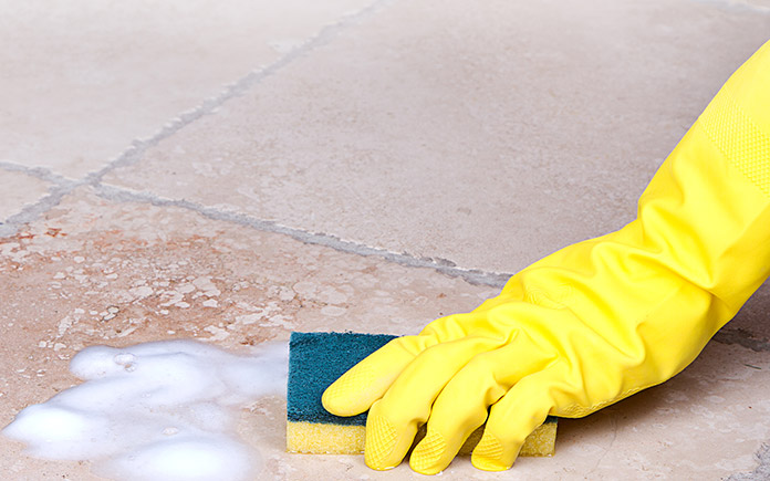 Gloved hand scrubbing ceramic tile floor with ammonia and liquid dish soap