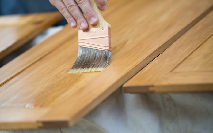 Paintbrush staining a wooden cabinet
