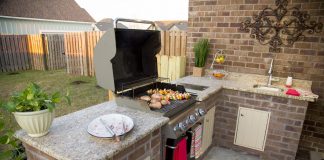 An outdoor kitchen area in a backyard, featuring a granite countertops, a grill and a sink