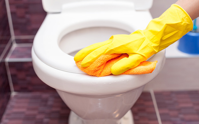 Yellow gloved hand cleaning the toilet seat