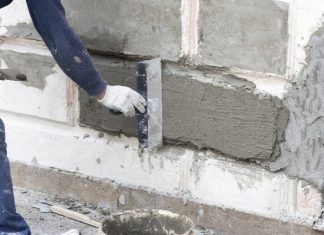 A person wearing white workmen gloves fixes the foundation of a home.