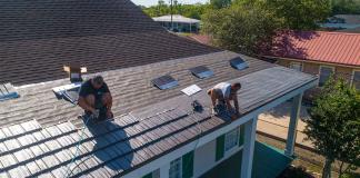 Workers lay metal roofing over an existing asphalt shingle roof