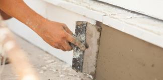 A person repairs the foundation of a home using plaster.