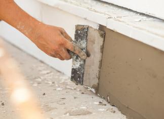 A person repairs the foundation of a home using plaster.