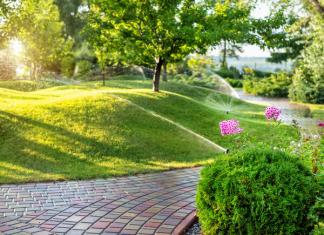 A green lawn with brick pathway through it and pink flowers with sprinklers running.