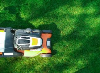 An orange lawn mower trimming green grass.