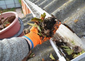 A person cleaning the gutters of a home while wearing orange gloves.