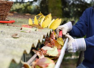 A professional wearing white gloves cleans fall leaves out of a gutter.